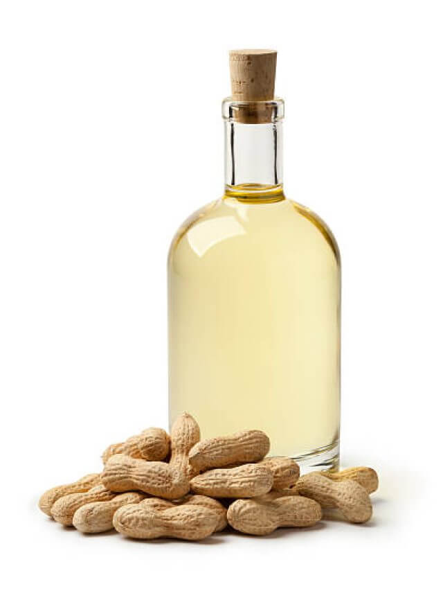 Bottle of peanut oil and peanuts on white background